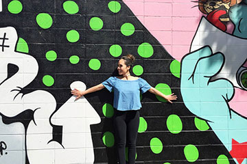 A girl poses in front of a wall covered with graffiti